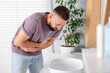 © New Africa - Man suffering from stomach ache and nausea over sink in bathroom
