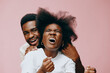 © SHOTPRIME STUDIO - Joyful African couple expressing excitement on a pastel pink background, showcasing natural hair and vibrant emotions in casual attire