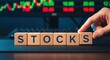 © deesignvalue - Wooden blocks spelling STOCKS a concept for stock market investment and trading with stock ticker in the background