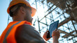 © CStock - A construction worker uses a tablet on site, showcasing modern technology in the building process under sunlight.