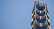© Margarita Ratatosk - Modern high rise building decorated with festive golden garland lights against a clear blue sky. Winter holiday season architecture.