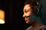 Teenage Black boy wearing gaming headset sitting indoors, concentrating on computer screen while playing video game, side profile showing focused facial expression