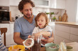 © Stockphotodirectors - A joyful father and his young child are spending quality time in the kitchen. They are engaged in a snack-making activity, sharing laughter and creating memories while surrounded by colorful bowls.