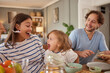 © Stockphotodirectors - Family shares a fun mealtime filled with laughter. Parents and child express happiness while enjoying food around a dining table in a warm, inviting kitchen.