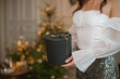 © RooM The Agency - Close-up side view of a glamorous woman in a party outfit standing in front of an illuminated Christmas tree holding a gift box