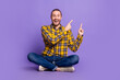 © deagreez - Young handsome guy in casual plaid shirt sits crosslegged on purple background pointing up for lifestyle fashion advert shopping campaigns