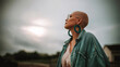 © Bonsales - Bald woman feeling empowered, looking upwards against a dramatic sky, symbolizing strength, overcoming challenges, and freedom