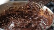 © VALENTYNA - Chocolate melting bowl with whisk creating dynamic splash motion dark melted mixture droplets flying culinary action studio lighting