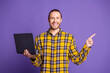 © deagreez - Young handsome man in checkered yellow shirt holds laptop and points to purple background