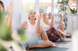 © JackF - Concentrated elderly woman sits on karemat, looks towards teacher and performs Lord of Fish asana by Ardha Matsyendrasan. People do hatha yoga in background