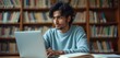 © miss irine - Indian student works on laptop in library. Man learns online using notebook with books. He studies at university using digital tech and cyberspace for call. Person works indoor on homework.