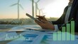 © Ch - Dynamic professional analyzing renewable energy growth charts on tablet with wind turbines in background at sunset, symbolizing green finance success
