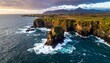 © KEPLEH - Rocky coastline with cliffs and mountain backdrop under cloudy sky, ocean waves crashing