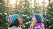 © Milan - Two diverse girls catching snowflakes on their tongues in winter. Happy African American and Causian friends playing outdoors in a snowy forest. Childhood friendship and fun