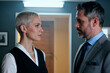 © DragonImages - Caucasian middle aged woman and Caucasian middle aged man standing face to face indoors, both maintaining serious expressions and making direct eye contact with each other