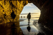 © Travel 'n' Lifestyle - View of a person silhouetted against the ocean framed by a golden cave entrance where the wet sand reflects the sky, Tongaporutu, Taranaki Region, New Zealand.