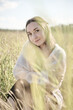 © TRAVELARIUM - Young woman sitting in sunlit rye field with soft-focus foreground