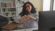 © Krakenimages.com - Young woman seated at desk types then forms heart with hands while smiling at computer in a building office; affection connection.