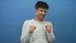 © Krakenimages.com - Man with clenched fists and eyeglasses standing in a studio setting against a vibrant blue backdrop; disgust.