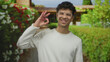 © Krakenimages.com - Young man smiles while making ok sign with hand at home entrance amid green leafy hedge and brick wall; approval.
