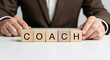 © Muhammad - Man arranges wooden blocks spelling 'coach' on a white surface representing guidance and support in business and personal development