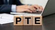 © Muhammad - Wooden blocks spelling pte with a person using a laptop in the background for pte exam preparation and educational resources online