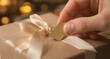 © Musfira - Close-up of a hand attaching a blank gift tag to a beautifully wrapped present with a satin ribbon, perfect for holiday or special occasion messages