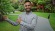 © Krakenimages.com - Man with bare hands pointing both index fingers to a park walkway beside a red building, smiling with open posture and pointing gesture; welcoming invitation.