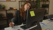 © Krakenimages.com - Caucasian woman in office looking stressed with computer and phone surrounded by work materials reflecting a busy workplace environment indoors.
