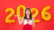© Bangkok Click Studio - Asian young cheerful woman smiling wear red dress, holding glass champagne sparkling posing with golden balloon shape number figure 2026 on red background, Happy New Year celebration festive holiday.