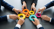 © abu - A group of hands connects colorful gears on a dark surface, symbolizing teamwork and business cooperation from a high angle perspective. Illustrates collaboration and solutions.