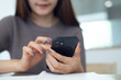 © tippapatt - Woman using mobile phone searching the information and taking note on notebook while working at home office, online business, teleworking, remote work concept. closeup