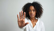 © Viktor - African American woman raises hand in stop gesture. Female shows hand in denial on white background. Black person protesting domestic violence. Fight against discrimination. Stop sign