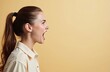 © Viktor - Young woman shouts with open mouth and wide eyes. Her side profile shows strong emotion. She wears a simple collared shirt against a plain beige backdrop.