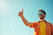 © Viktor - Man with thumbs up and sunglasses smiles against blue sky. He wears orange floral shirt and yellow t shirt. Looks happy, successful, confident. Copy space for text.