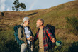 © sashafolly - Elderly man supports wife on weekend hike at hilly autumn countryside