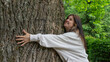 © SlepoyKot - Joyful Young Woman Happily Hugging a Large Tree Trunk, Expressing Love and Connection with Nature in a Green Park.