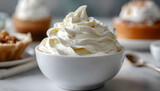 Close-up of vanilla soft serve ice cream swirled in a white bowl, placed on a table with other desserts in the background.