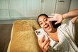 © Marko Geber - Adult woman laughing while video calling on sofa at home