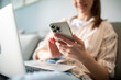 © Davor - Young adult woman smiling using smartphone and laptop at home