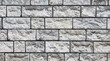 © Martins - Close-up of a gray stone wall made of rectangular blocks with rough, uneven surfaces and visible mortar lines, creating a textured architectural pattern.