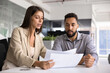 © fizkes - Serious young Latin business professional woman explaining paper to coworker