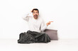 © luismolinero - Caucasian man in pajamas sitting on the floor at indoors surprised and pointing finger to the side