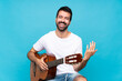 © luismolinero - Young man with guitar over isolated blue background smiling a lot