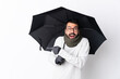 © luismolinero - Caucasian handsome man with beard holding an umbrella over isolated white wall surprised and pointing finger to the side