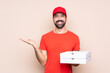 © luismolinero - Young man holding a pizza over isolated background holding copyspace imaginary on the palm to insert an ad