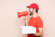 © luismolinero - Young man holding a pizza over isolated background shouting through a megaphone