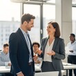 © Nazmus - Business colleagues smiling and talking in a modern office with other coworkers in the background near window