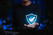 © Supatman - Person holding glowing digital shield with check mark icon representing online security, safety, cybersecurity assurance, insurance, trust, data protection, authentication, verified system, compliance