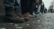 © Willy AS - A ground-level view of people's legs and worn footwear as they stand in a long, patient line on a gritty city pavement